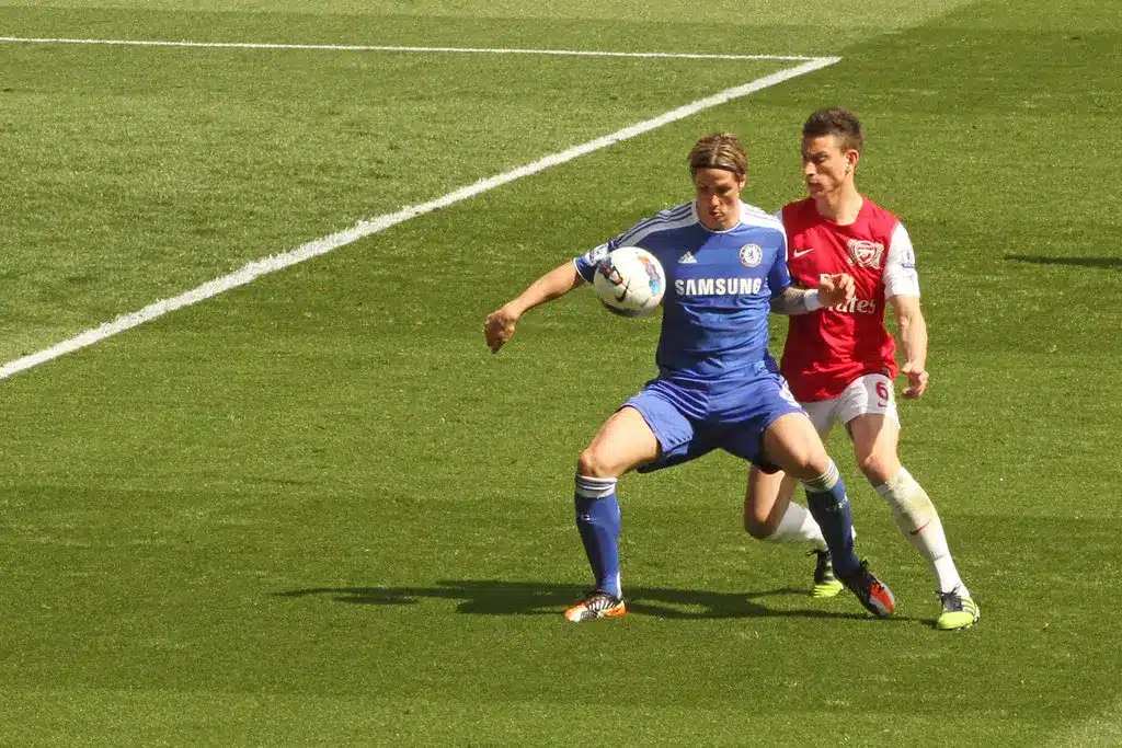 Fernando Torres sous le maillot bleu de Chelsea contrôle un ballon de football avec Laurent Koscielny derrière lui.